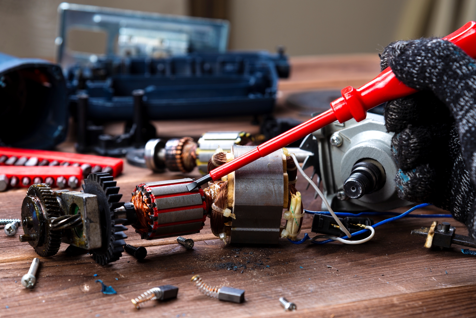 the master repairs a broken electrical device: drill, cutter on a wooden table. Electric Tool Repair Shop